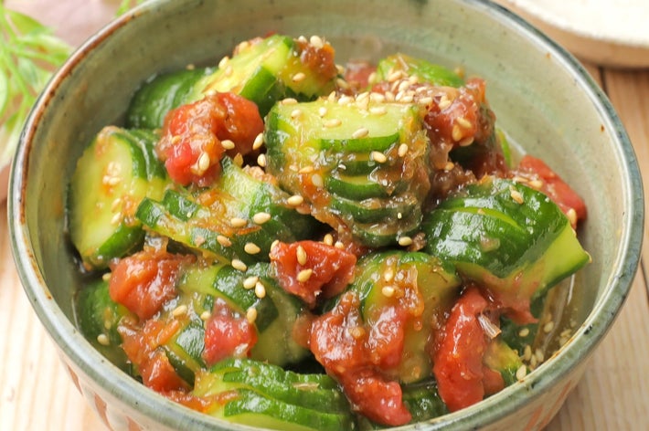 ゴマとトマトを添えたキュウリの和え物が器に盛られている。シンプルで美味しそうな野菜料理。