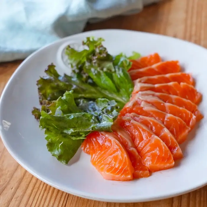 皿に盛られた新鮮なサーモンの刺身とレタスの葉。