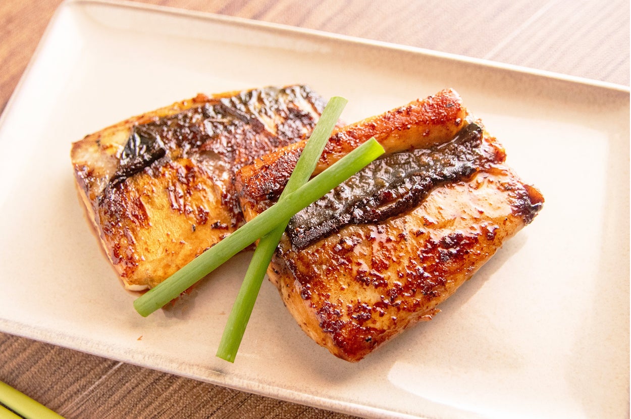 白い皿に盛られた焼き魚の切り身2枚、上にネギが添えられている。