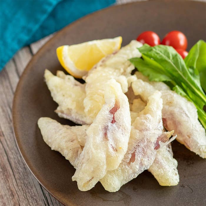 レモンとトマト、葉野菜を添えた魚の天ぷらが皿に盛られている。