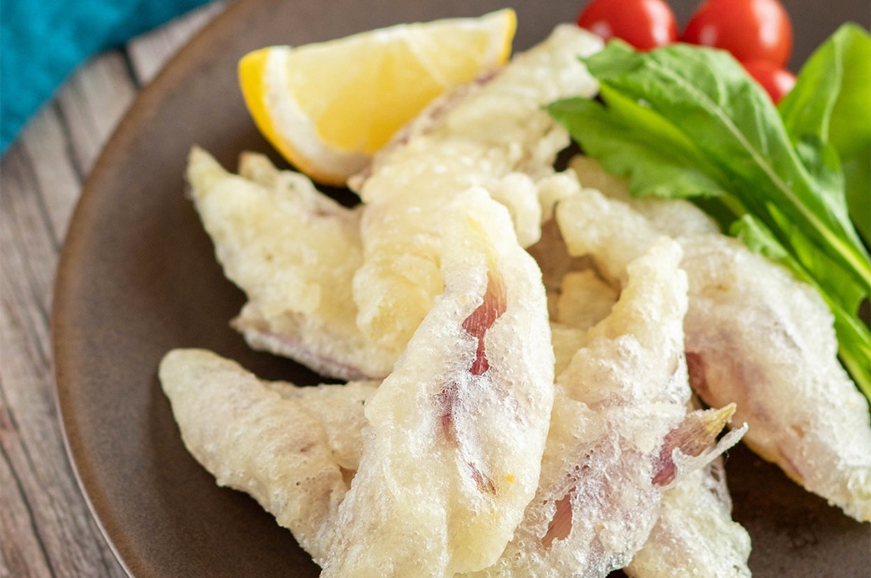 魚の天ぷら、レモンのスライス、トマト、葉野菜が皿に盛られている。