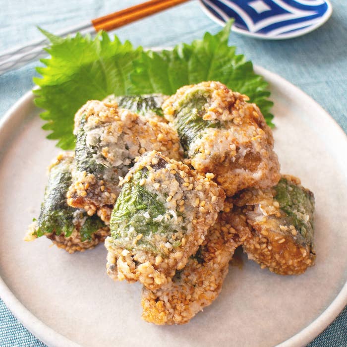 お皿に盛られた揚げ餃子風の料理。大葉で包まれ、ゴマがまぶされています。後ろに箸と青い模様の皿が見えます。