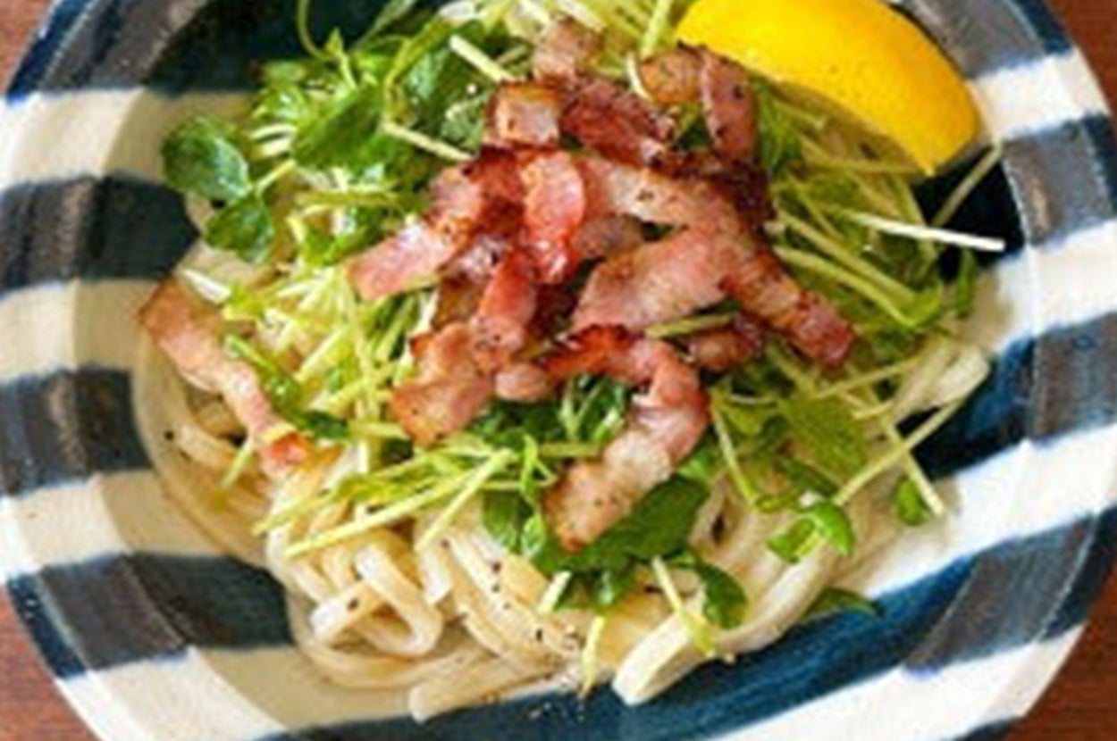 器に盛られたカルボナーラうどん。ベーコンとクレソンがトッピングされ、レモンが添えられている。