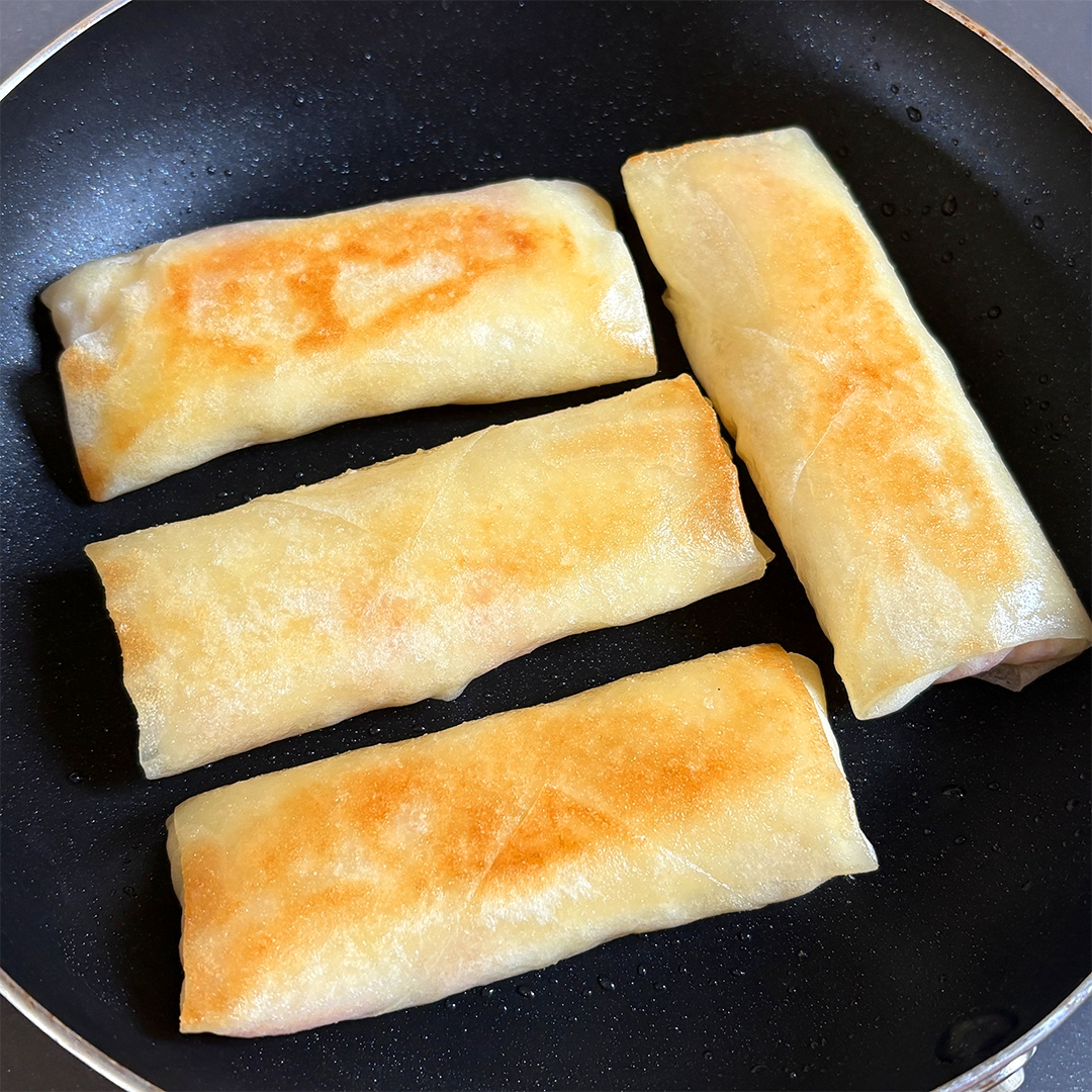 フライパンで焼かれている4つの春巻きが見える。