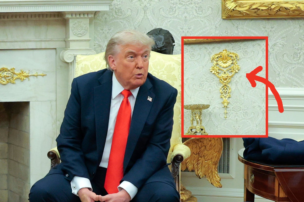 A person in a suit and red tie sits in an ornate room with a focus on a decorative gold embellishment on the wall