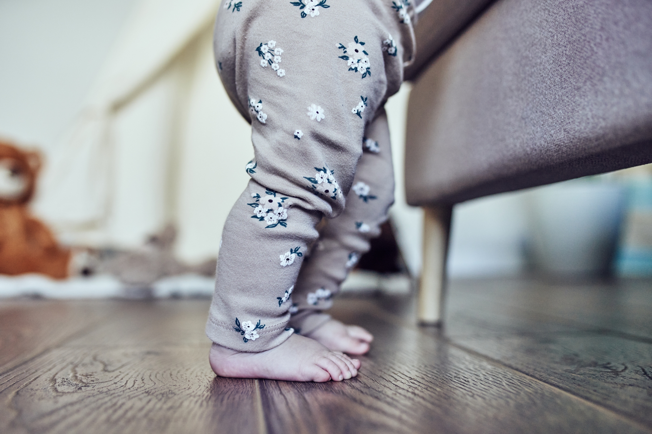Baby i blomstermønstrede leggings står på tipper ved en stol på tregulv