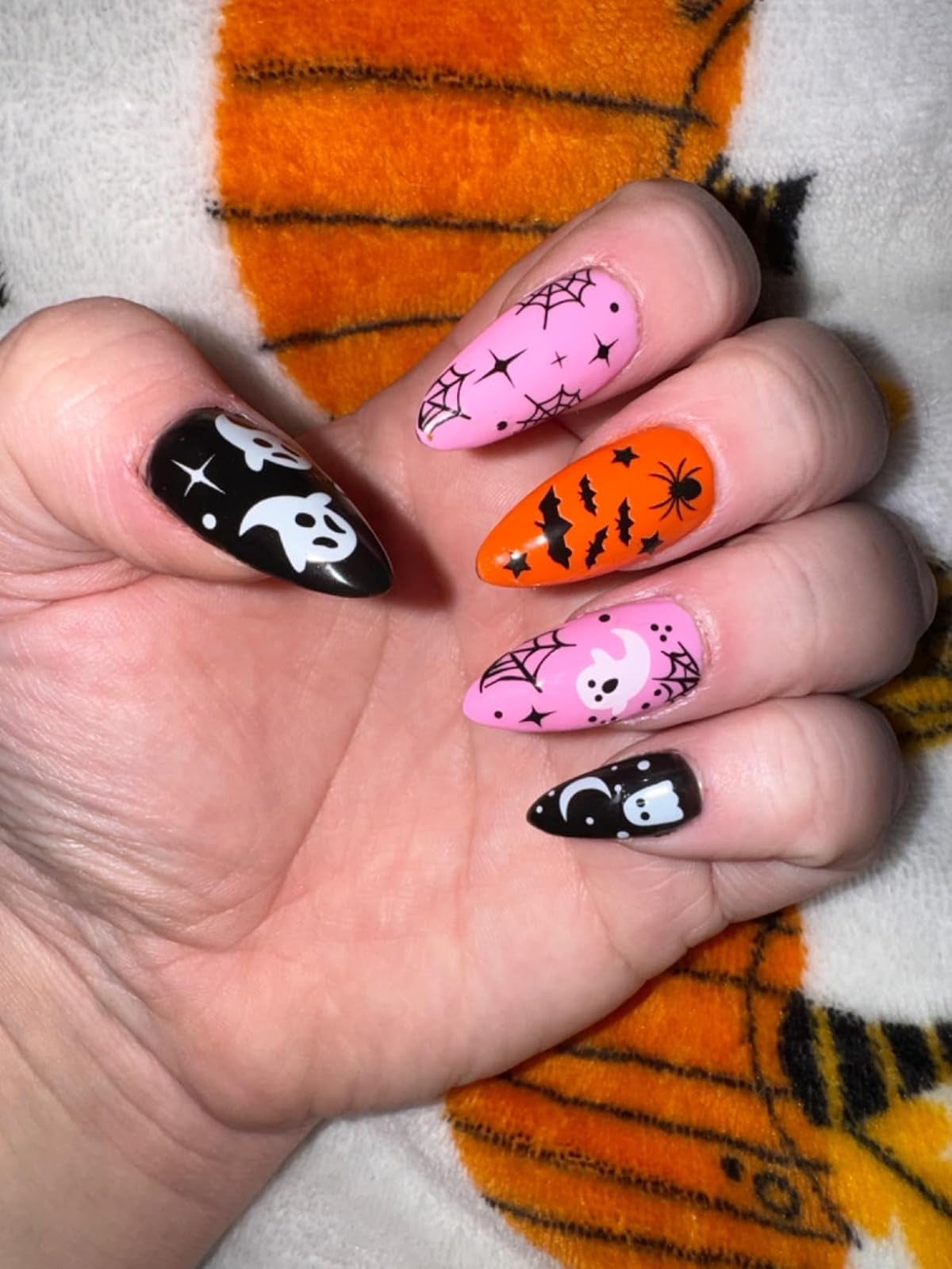 Hand with Halloween-themed nail art featuring ghosts, spiders, bats, and web designs on various nails.