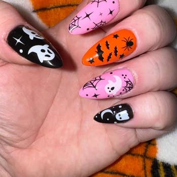 Hand with Halloween-themed nail art featuring ghosts, spiders, bats, and web designs on various nails.