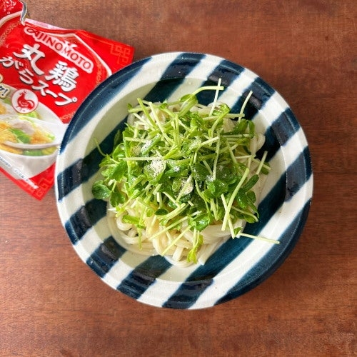 おしゃれなデザインの皿に盛り付けられた麺料理、上にはたっぷりの野菜がトッピングされている。隣にはスープのパッケージ。