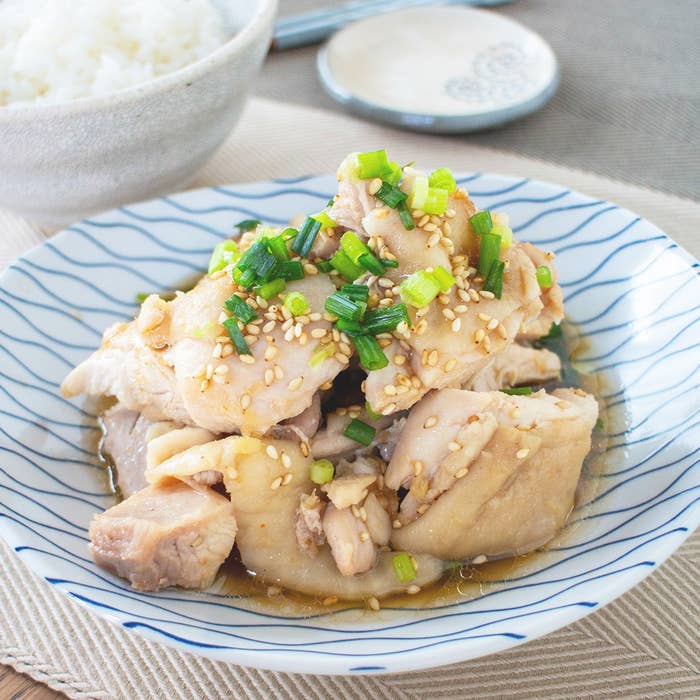 皿に盛られた鶏肉の料理、ネギとゴマが飾られています。背景にご飯と小皿が見えます。