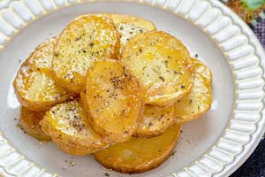 じゃがいもスライスが皿に盛られ、胡椒がかけられた料理。背景にテーブルクロスと観葉植物が見える。