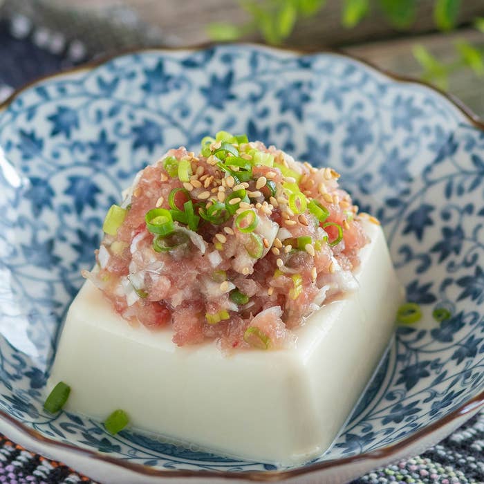 器に盛られた寄せ豆腐には、ネギとゴマがトッピングされている料理。