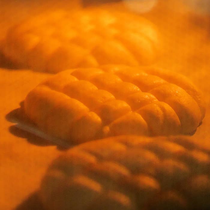 パンがオーブンで焼かれている様子。メロンパンの表面がふっくらと膨らんでいる。