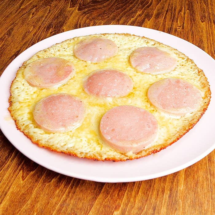 白い皿に盛られた丸いチーズピザの上に薄くスライスされたソーセージが均等に並べられています。