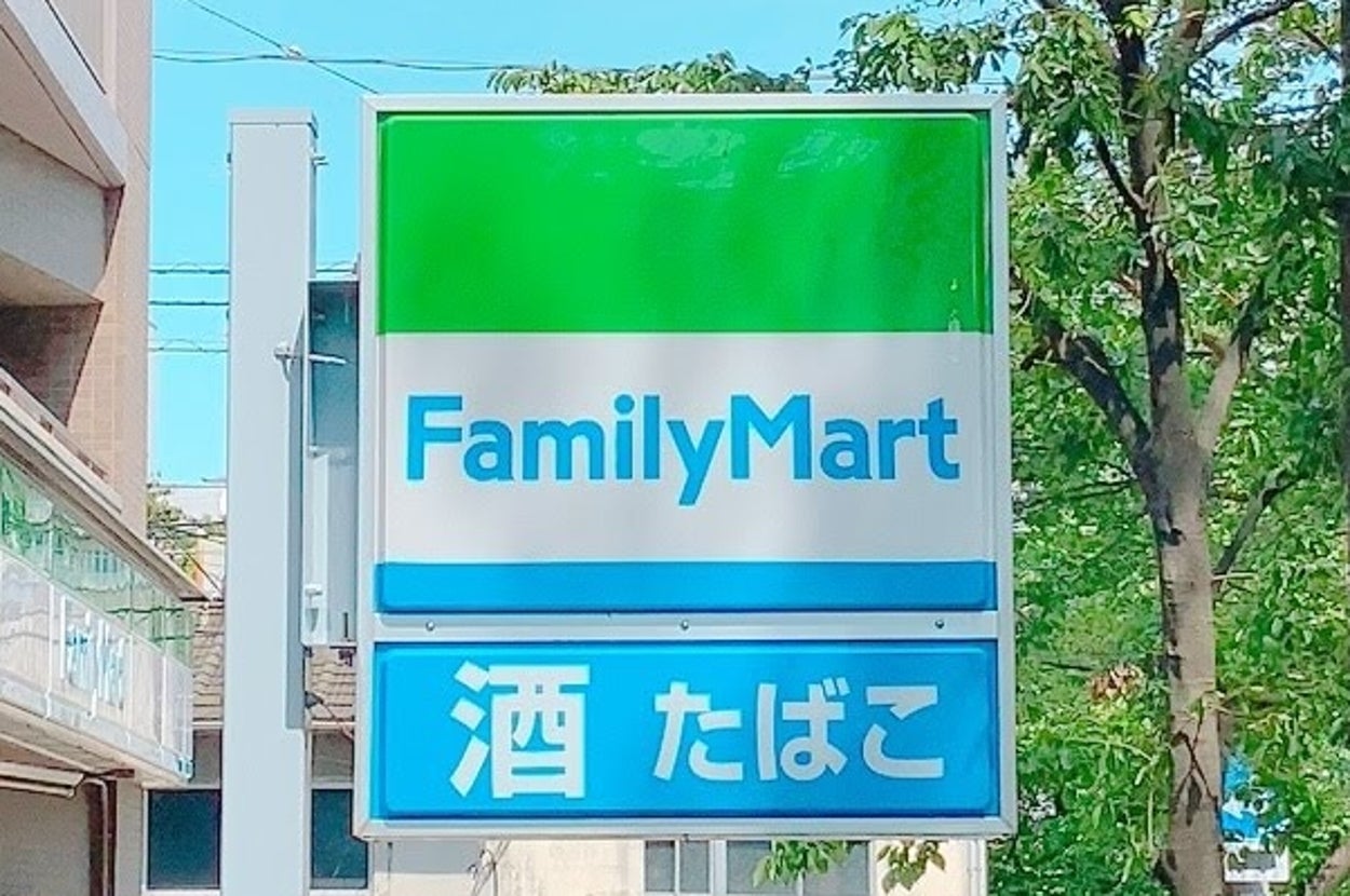 ファミリーマートの看板が通りに立っている。周囲に木と建物が見える。