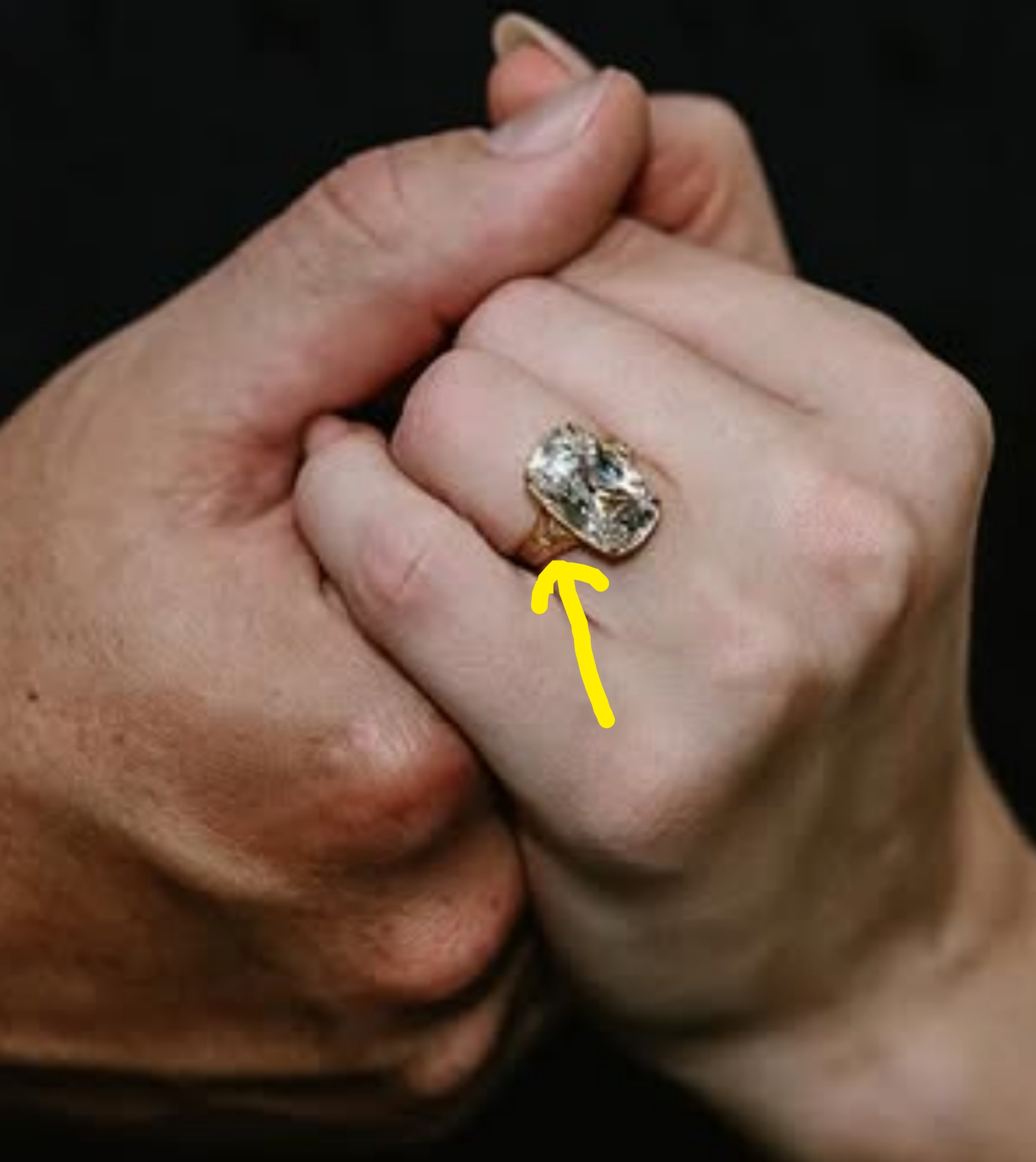 Two hands clasped together, one wearing a large diamond ring