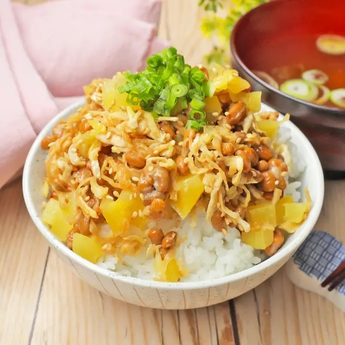 納豆とたくあんの乗ったご飯の丼がテーブルに置かれている。味噌汁が横にある。