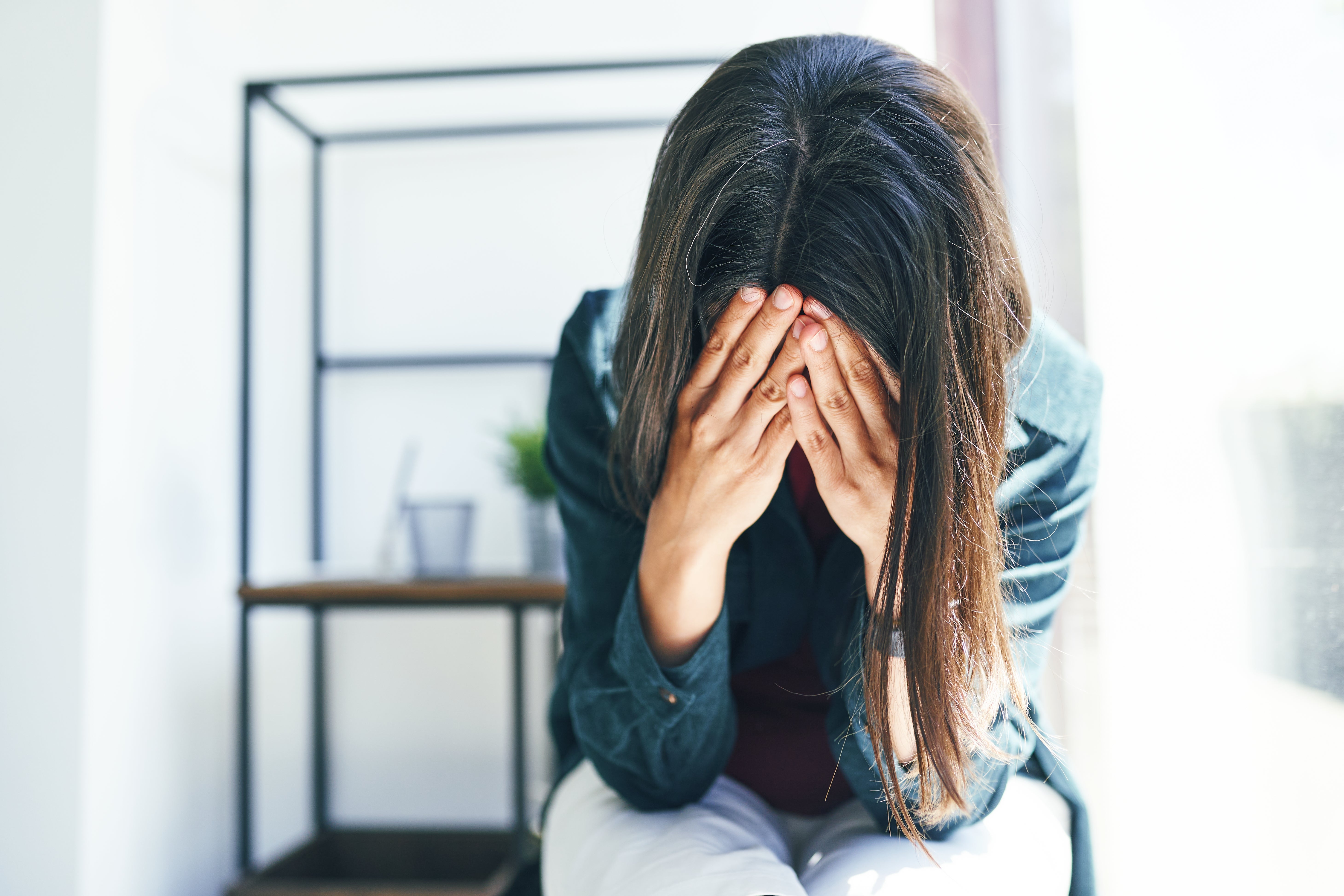 Person som sitter med hodet i hendene, virker bekymret, i et rom med en hylle i bakgrunnen