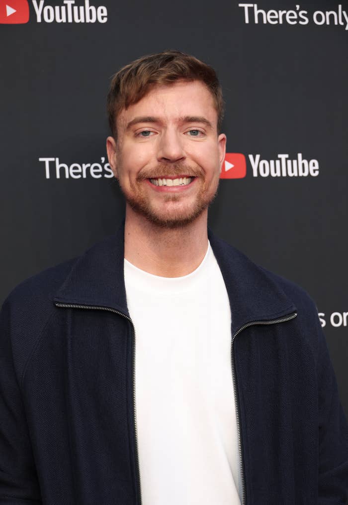 Person smiling astatine an lawsuit backdrop with YouTube logos wearing a casual overgarment implicit a plain shirt