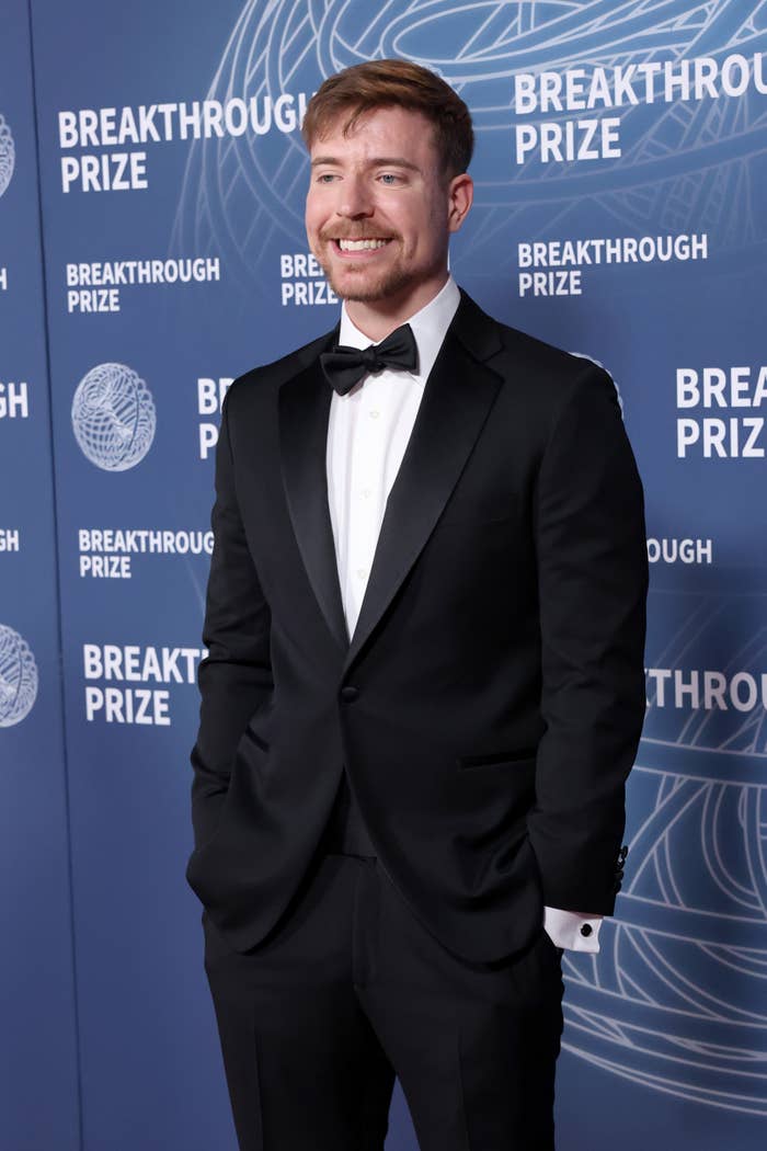 Person successful a tuxedo smiling astatine a Breakthrough Prize event, lasting against a backdrop with lawsuit logos