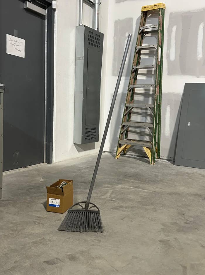 A broom propped up connected a factual level adjacent to a cardboard container and a gangly ladder successful an unfinished space