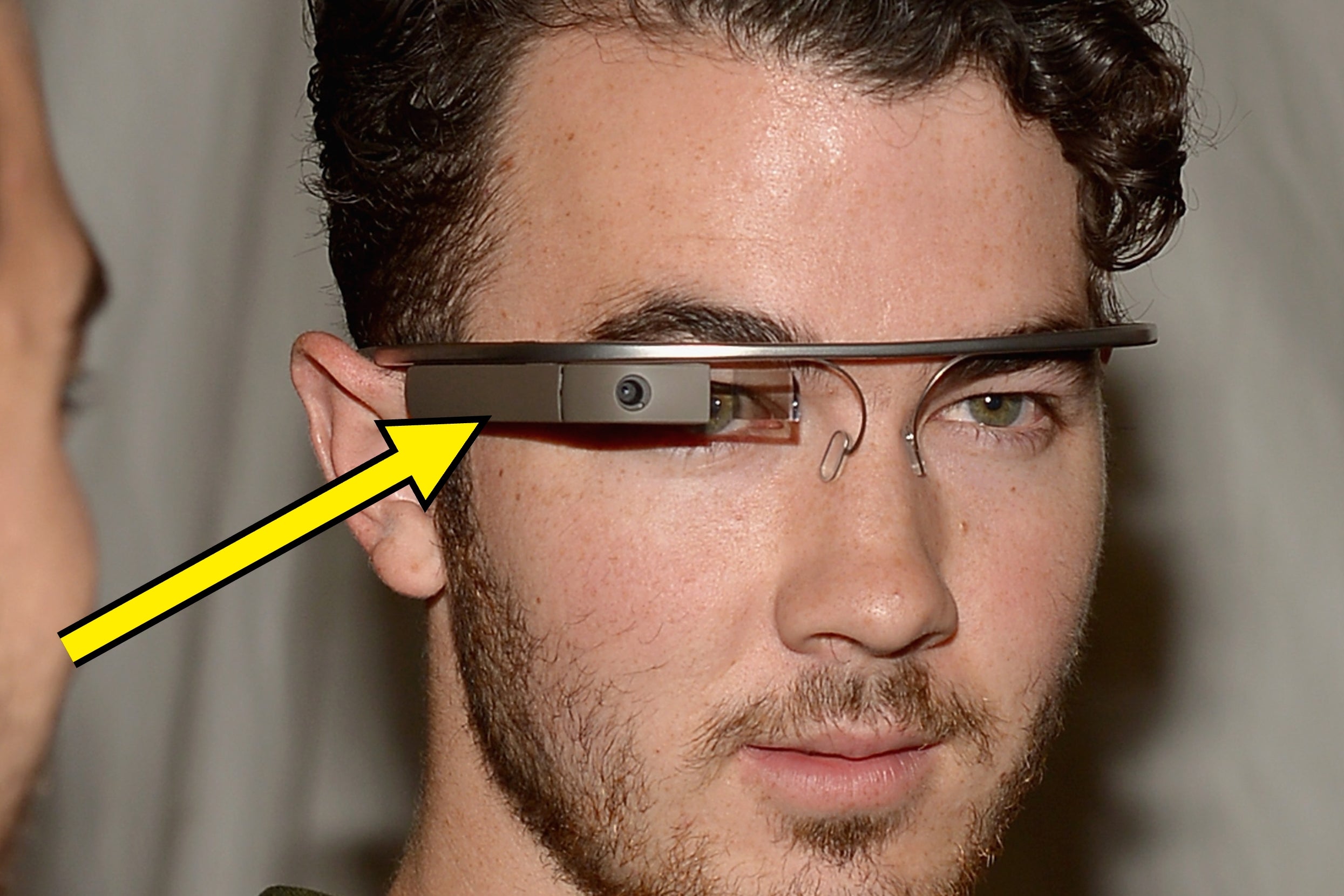 Person wearing augmented reality glasses with a yellow arrow pointing towards them, suggesting focus on the device