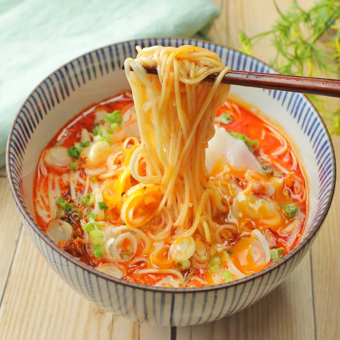 丼に盛られたそうめんを箸で持ち上げる。ネギや卵がトッピングされたスープが見える。