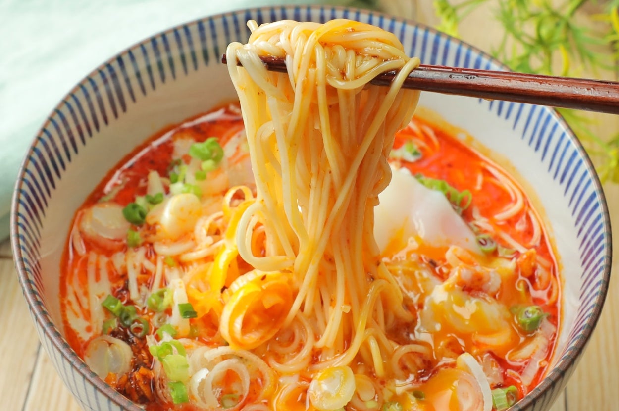 箸で持ち上げられた麺の入ったラーメンの丼、トッピングにはネギや卵が見える。