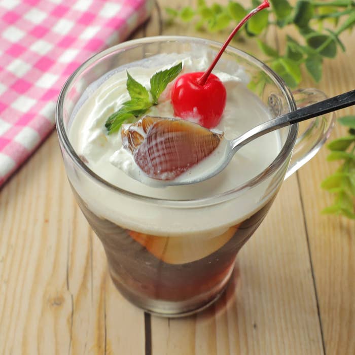 コーヒーゼリーの上にクリームとチェリーがのったデザートがガラスのカップに入っている。スプーンで一口すくわれている。