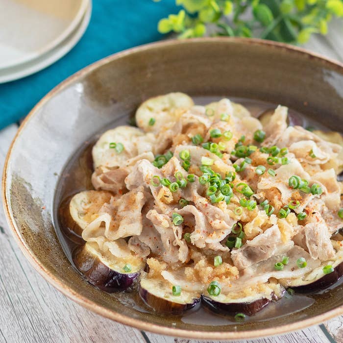 ボウルに盛り付けられた豚の薄切り肉と野菜の料理。上にネギとソースがかかっている。