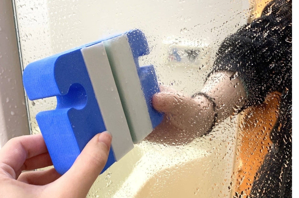 手に持った清掃用具で窓ガラスを拭いている様子。ガラスには水滴がついている。
