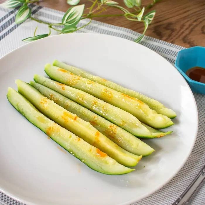 白い皿にスライスされたズッキーニが並び、上に調味料がかかっています。隣に青い小皿が置かれています。