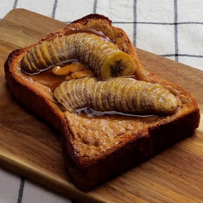 厚切りトーストにピーナッツバターとスライスされたバナナがのせられた食事の写真。木のプレートに置かれている。