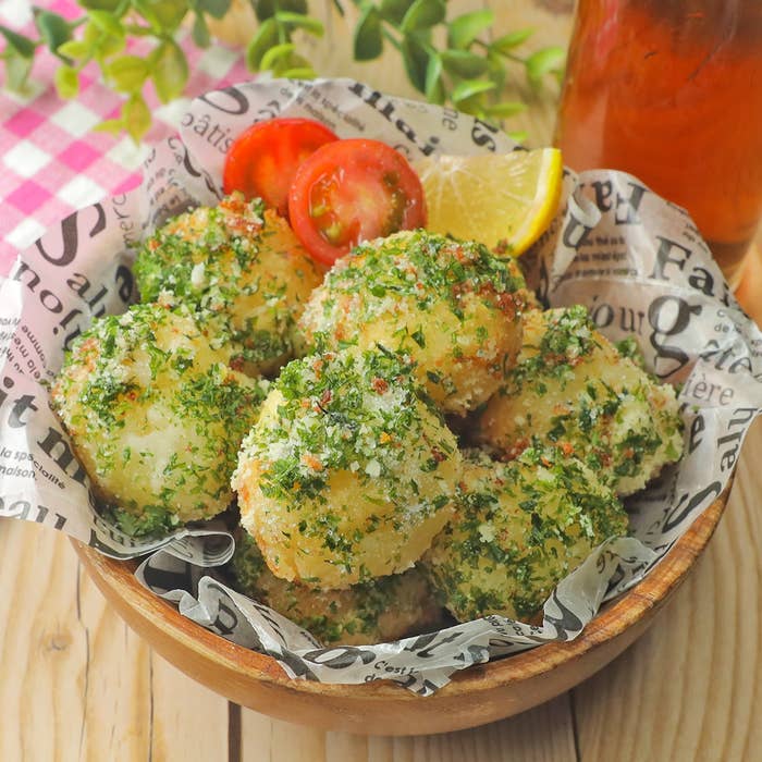 木製のボウルに盛られたハーブやパン粉がかかった複数のポテトボール。レモンスライスとトマトが添えられています。
