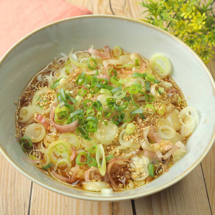 ネギとゴマがトッピングされた麺の入った料理が浅いボウルに入っている。