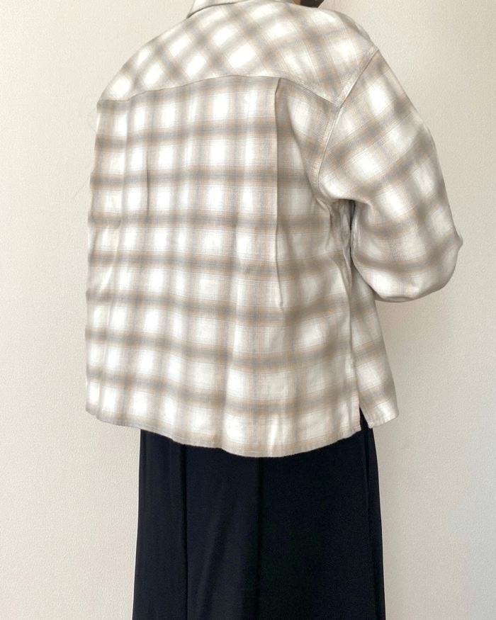 Person wearing a plaid shirt with loose fit, seen from the back, paired with dark pants against a plain background