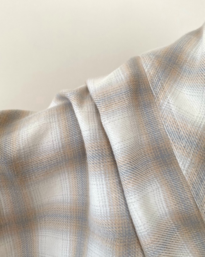 Close-up of a soft, folded plaid fabric with a subtle check pattern, showing texture and drape