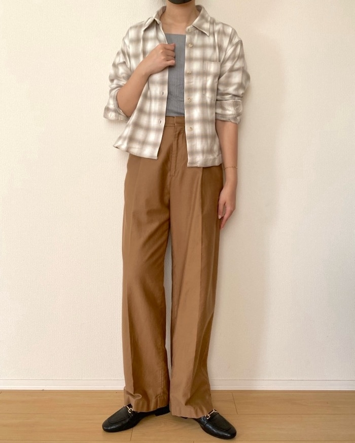 Person standing against a plain wall, wearing a plaid shirt over a top, and wide-legged pants, with loafers
