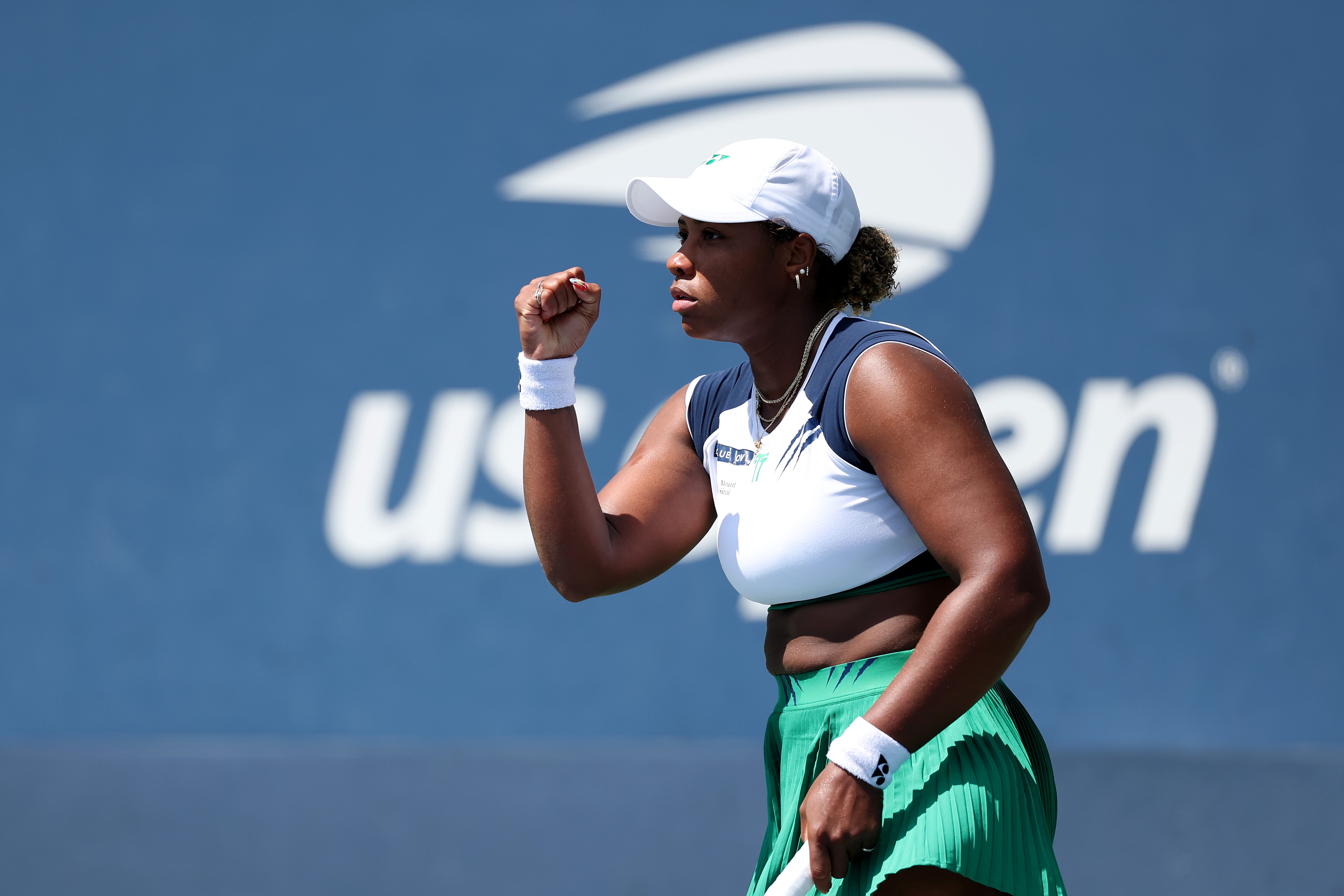 Tennis player celebrates a point at the US Open, wearing a sporty green skirt and white visor