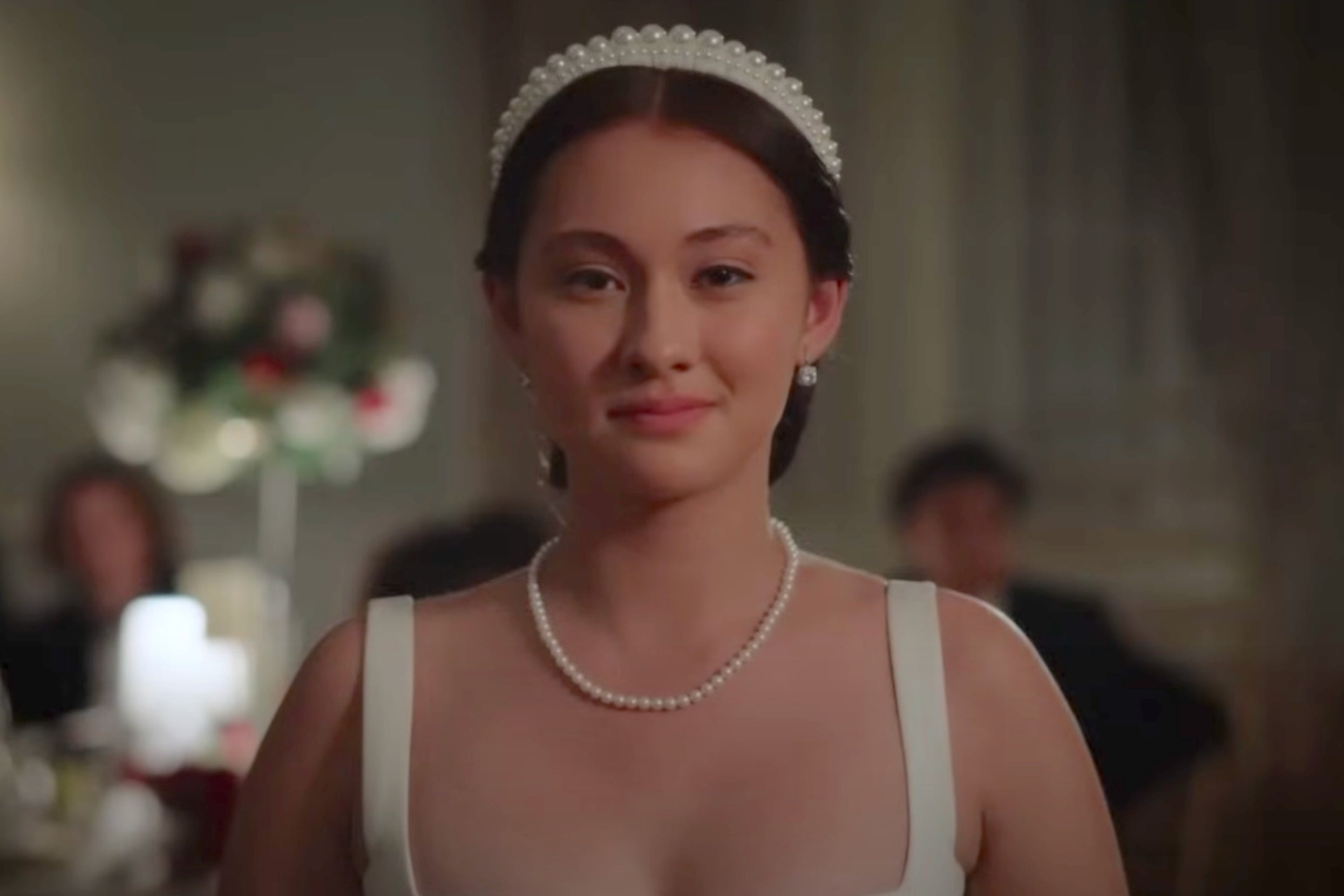 Belly from The Summer I Turned Pretty wearing a sleeveless dress and pearl necklace in a formal setting, with a soft, confident expression