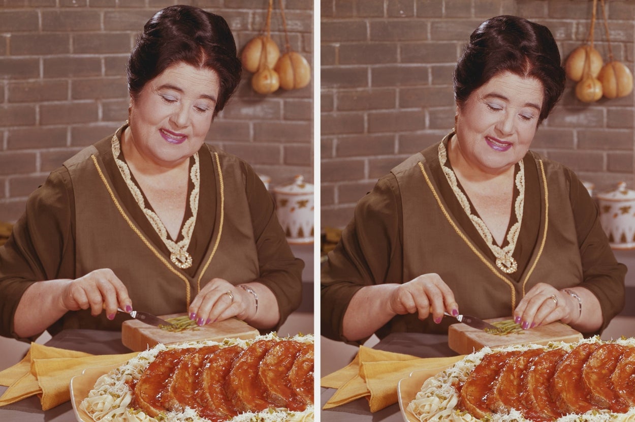 A person in a kitchen preparing a dish with sliced meat and pasta on a cutting board, with hanging onions in the background