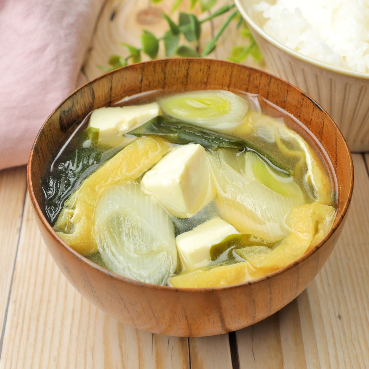 味噌汁の写真。豆腐、ネギ、わかめなどの具が入っている。奥に白いご飯が少し見える。