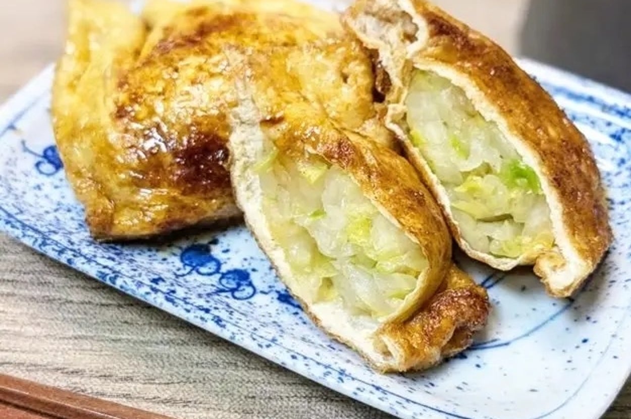 油揚げに巻かれたキャベツと豆腐の焼き物が小皿に乗せられ、横に箸が置かれています。