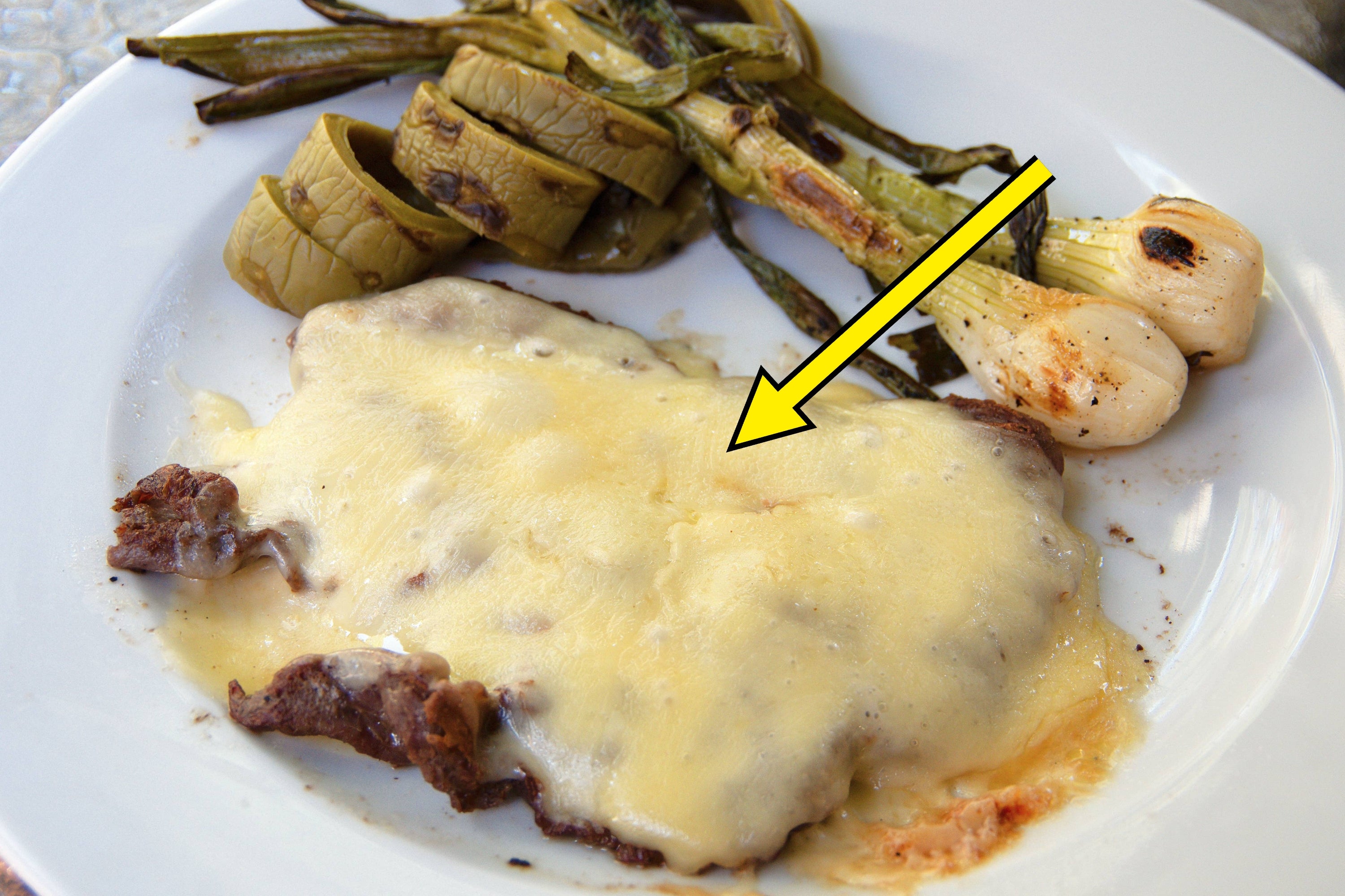 Melted cheese over steak with grilled green peppers and onions on a white plate