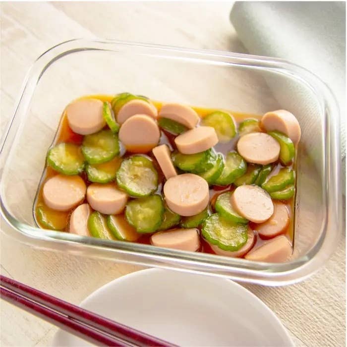 ガラスの容器に盛られたソーセージときゅうりを和えた料理。食卓にははしの準備がされている。