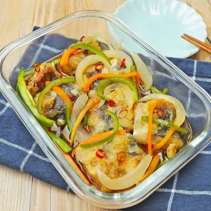 ガラス皿に並べられた調理済みアジの南蛮漬け。野菜のトッピング付き。