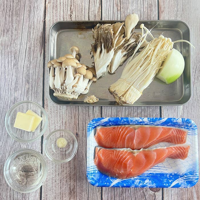 サーモンの切り身、シメジ、エノキなどのきのことタマネギがトレーに並べられている料理の準備シーン。