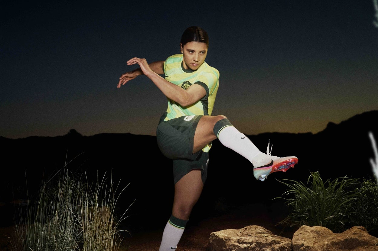 Soccer player in action, mid-kick, wearing sports uniform and cleats, on a grassy terrain at dusk