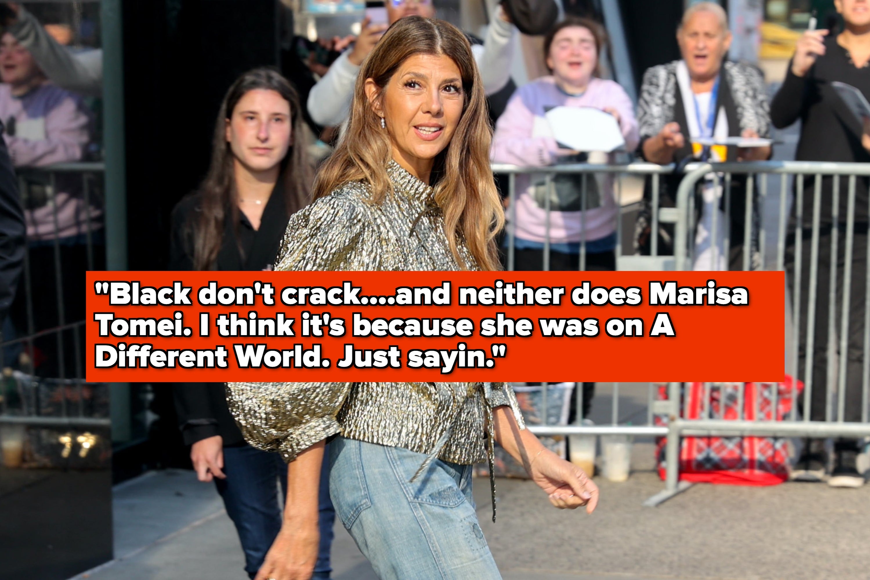 Marisa Tomei, wearing a metallic blouse and pants, walks past a crowd. Text over the image humorously comments on her youthful appearance