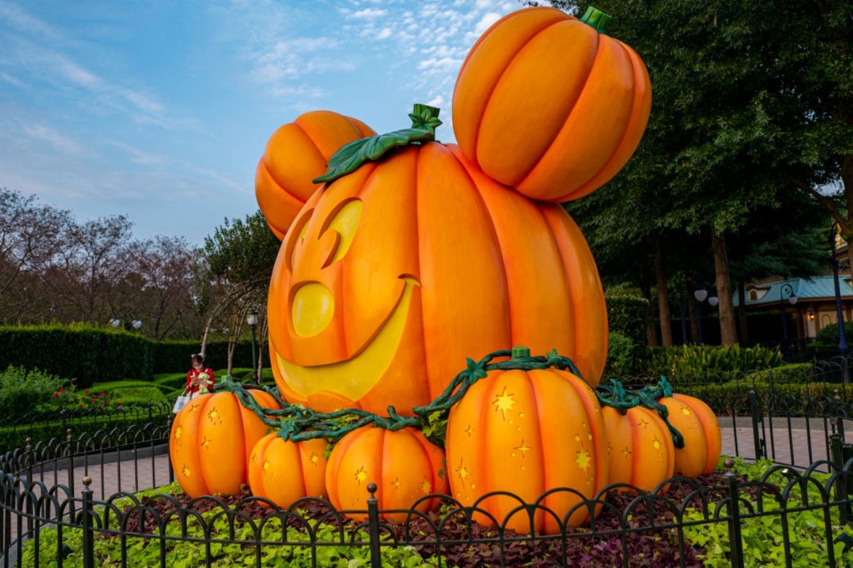 Giant pumpkin sculpture with Mickey Mouse ears, surrounded by smaller pumpkins in a garden setting